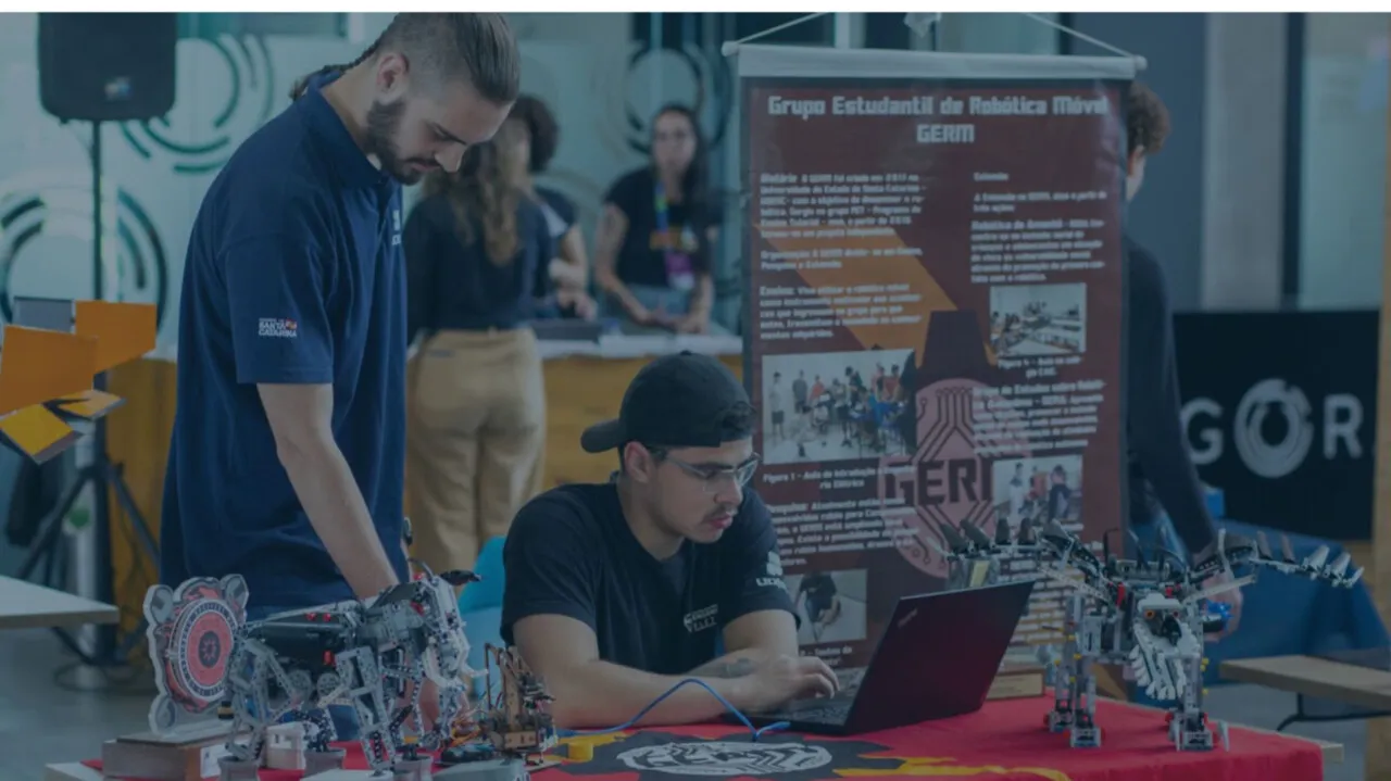 Estudantes do grupo de robótica móvel GERM trabalham em robôs e em um notebook no estande do grupo durante um evento