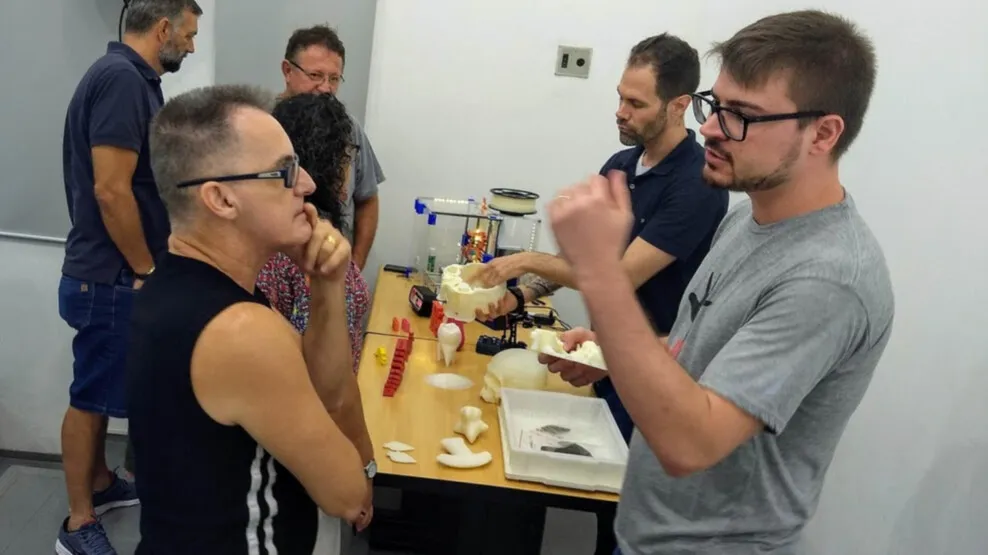 Visitantes conversam em volta de uma mesa com réplicas arqueológicas impressas em 3D.