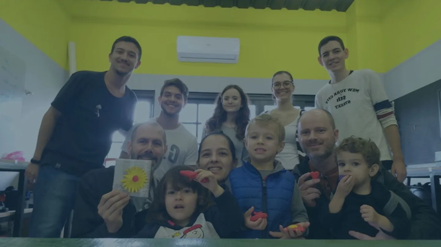 Voluntários do Fab Lab Joinville reunidos com crianças e famílias, que mostram as peças feitas em uma oficina.