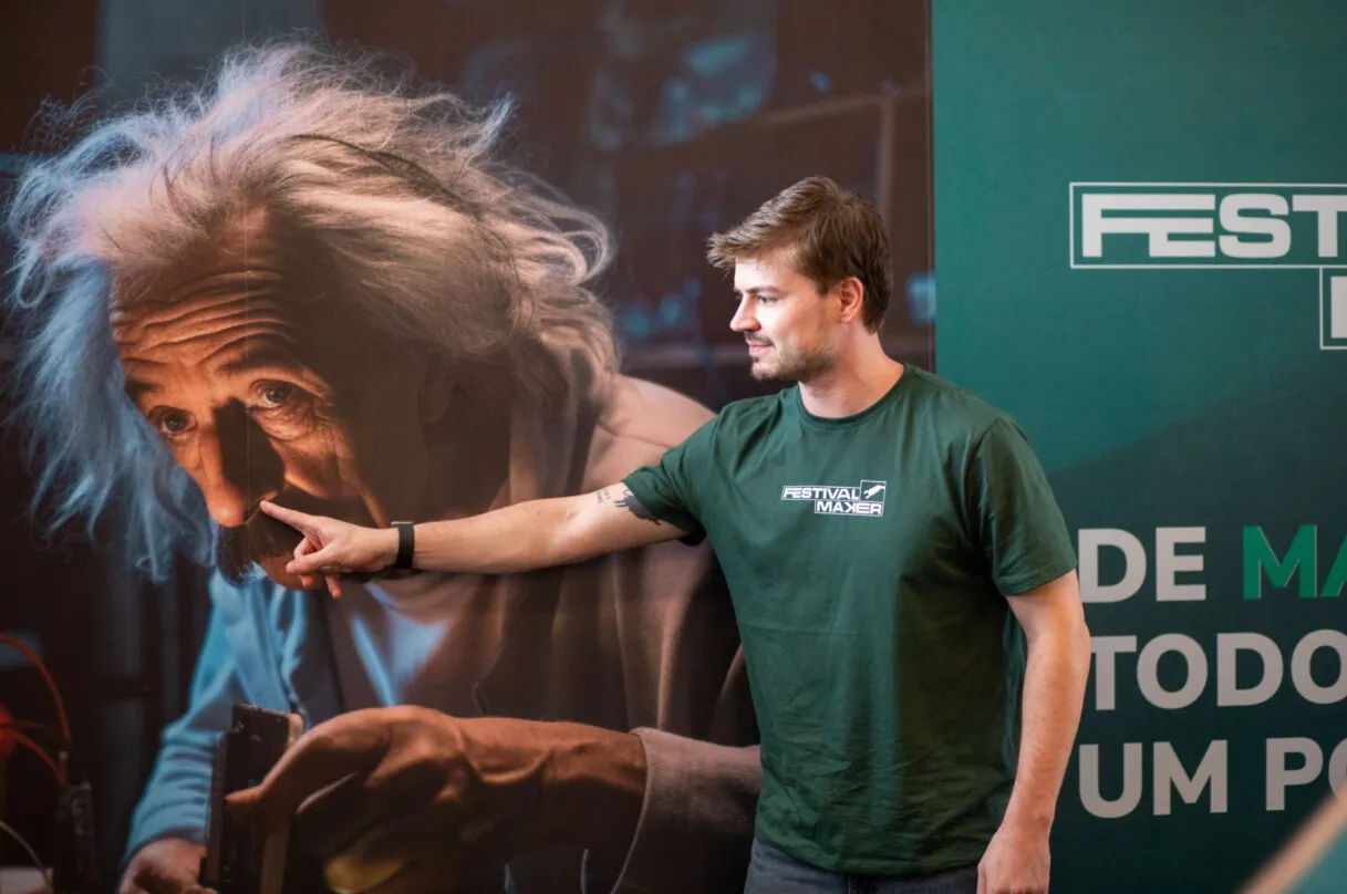 Participante com camiseta do Festival Maker aponta para um painel com o rosto de Albert Einstein durante o evento