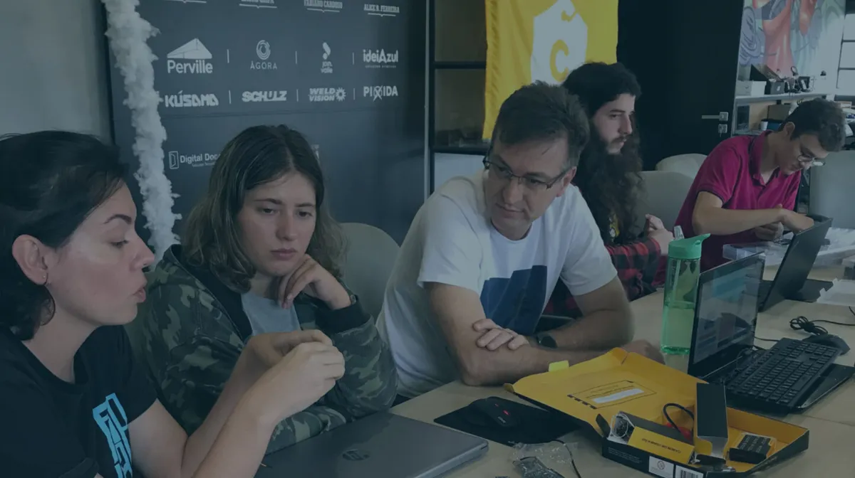 Pessoas reunidas em uma mesa do Fab Lab Joinville, trabalhando com notebooks e componentes eletrônicos.