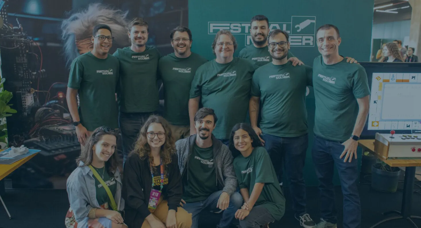 Equipe de voluntários com camisetas verdes do Festival Maker posa sorrindo em frente ao estande do evento