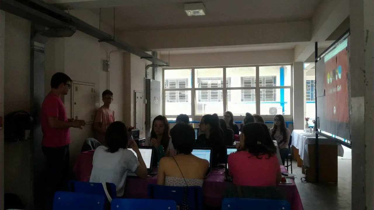 Sala com participantes do Code like a girl diante dos notebooks, acompanhando uma explicação ao lado da projeção.