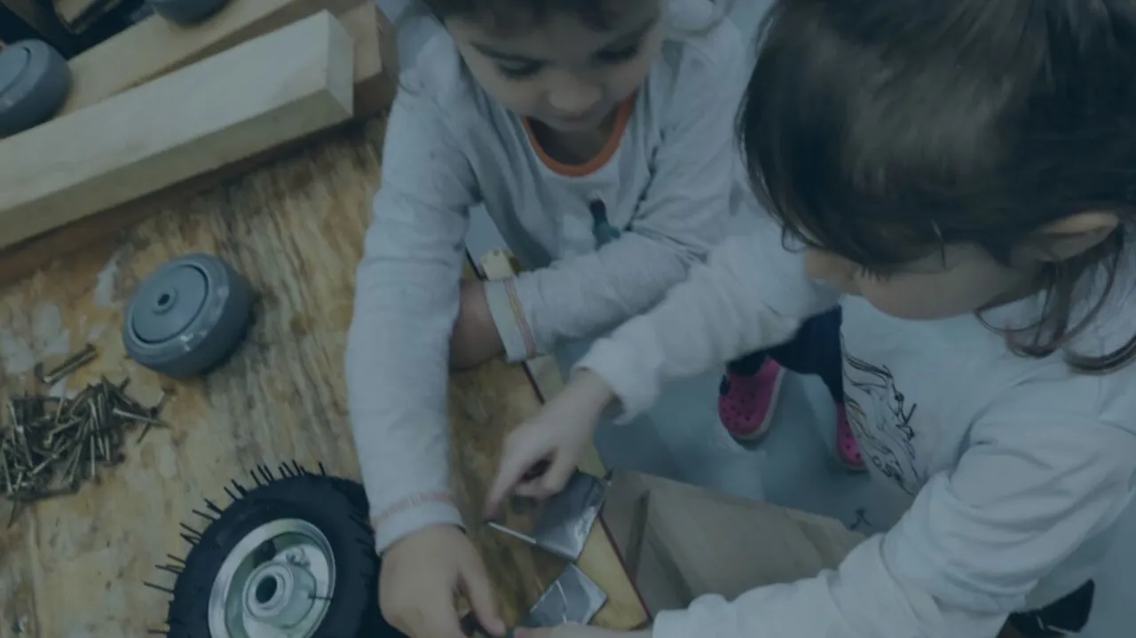 Duas crianças montando um carrinho de madeira com rodas e pregos em uma bancada do Fab Lab