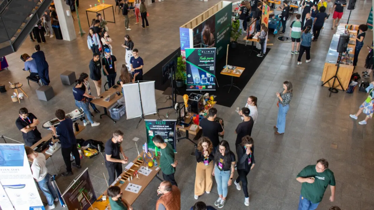 Vista do alto do Festival Maker: estandes de equipes e startups em um grande saguão com visitantes circulando.