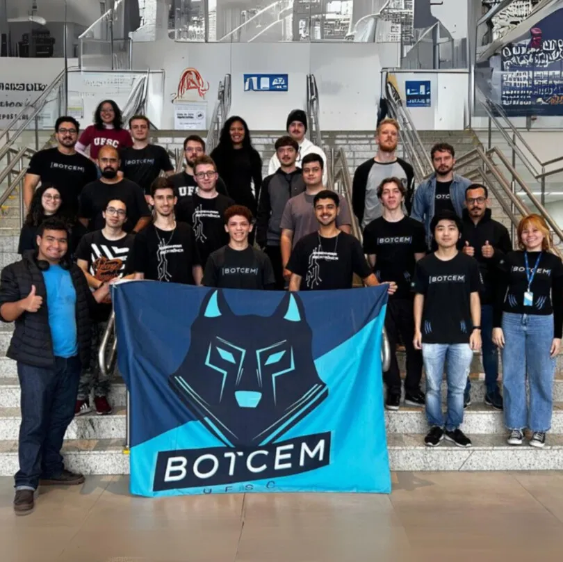 Integrantes da equipe de robótica Botcem posam em uma escadaria segurando a bandeira azul da equipe, com um lobo estilizado.
