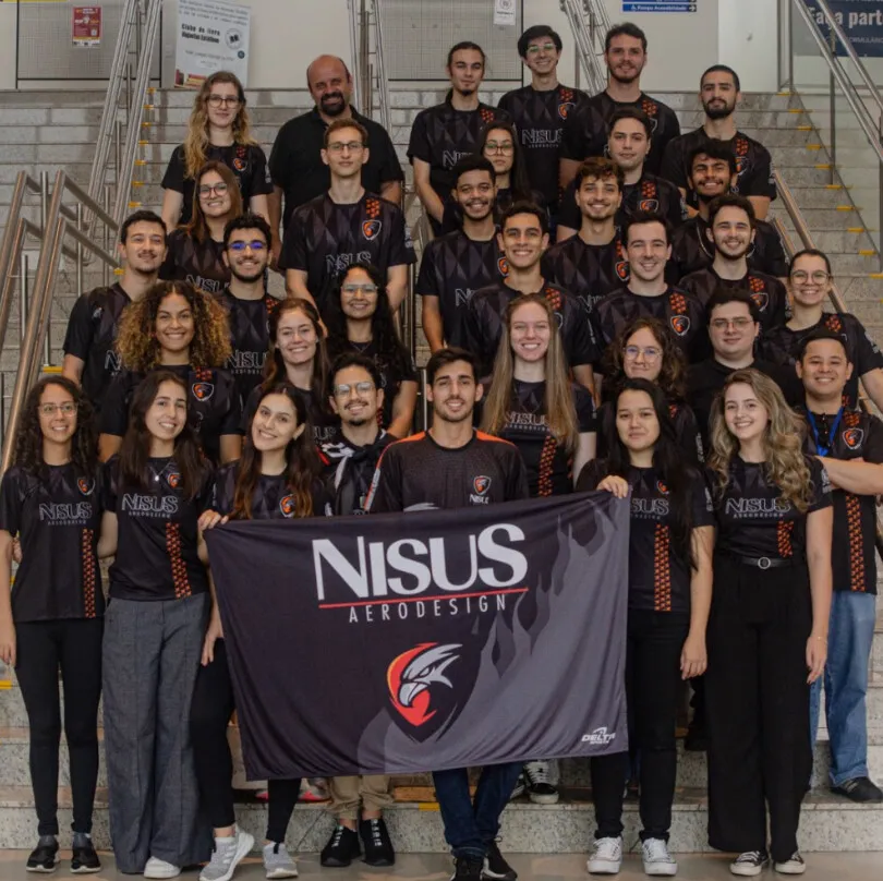 Integrantes da equipe Nisus Aerodesign posam em uma escadaria segurando a bandeira da equipe.