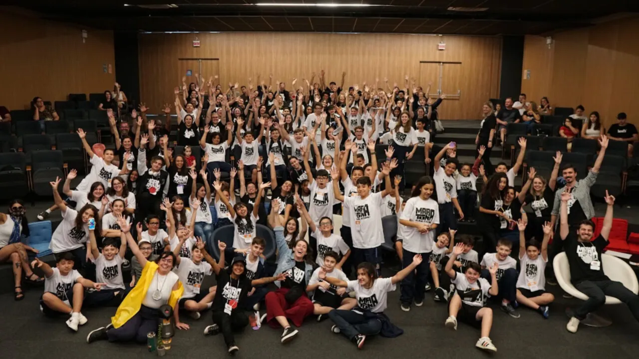 Estudantes e professores da rede municipal comemoram de braços erguidos em um auditório durante a Maratona Lab Code.
