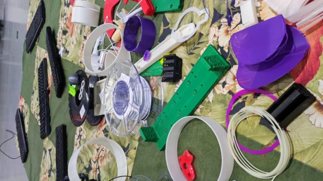 Objetos de plástico colorido, carretéis de filamento e peças diversas espalhados sobre um tecido estampado.
