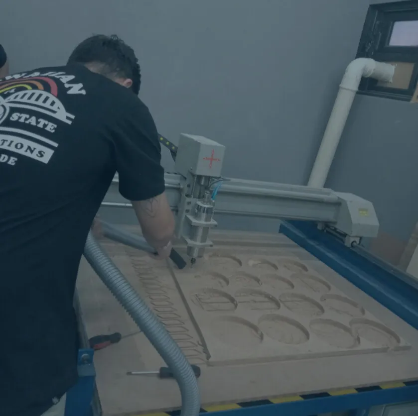 Pessoa acompanhando a fresa CNC enquanto ela usina peças circulares em uma chapa de madeira