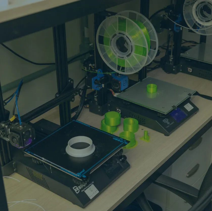 Impressoras 3D de filamento lado a lado na bancada, com peças verdes recém-impressas