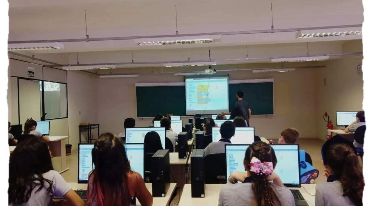 Laboratório de informática com alunos nos computadores enquanto o Scratch é projetado no quadro.