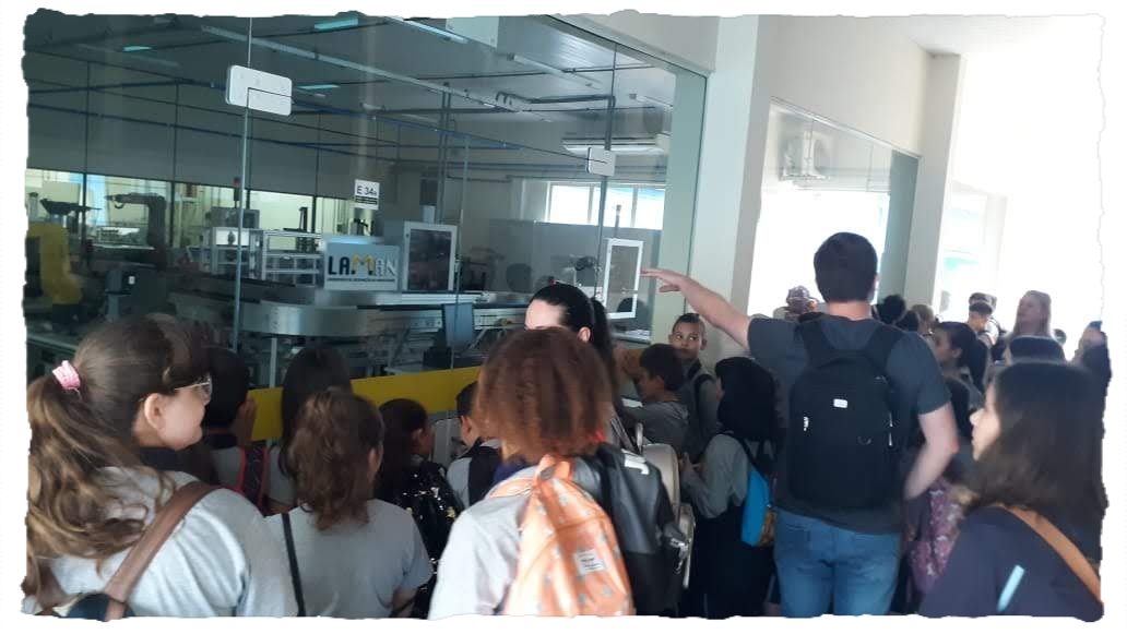 homem apontando para o laboratorio de robotica enquando as crianças olham os equipamentos